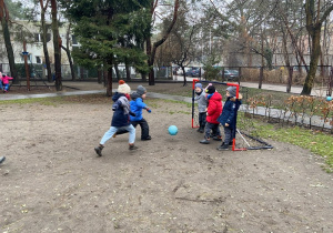 Chłopiec strzela gola. Na bramce stoi trójka dzieci